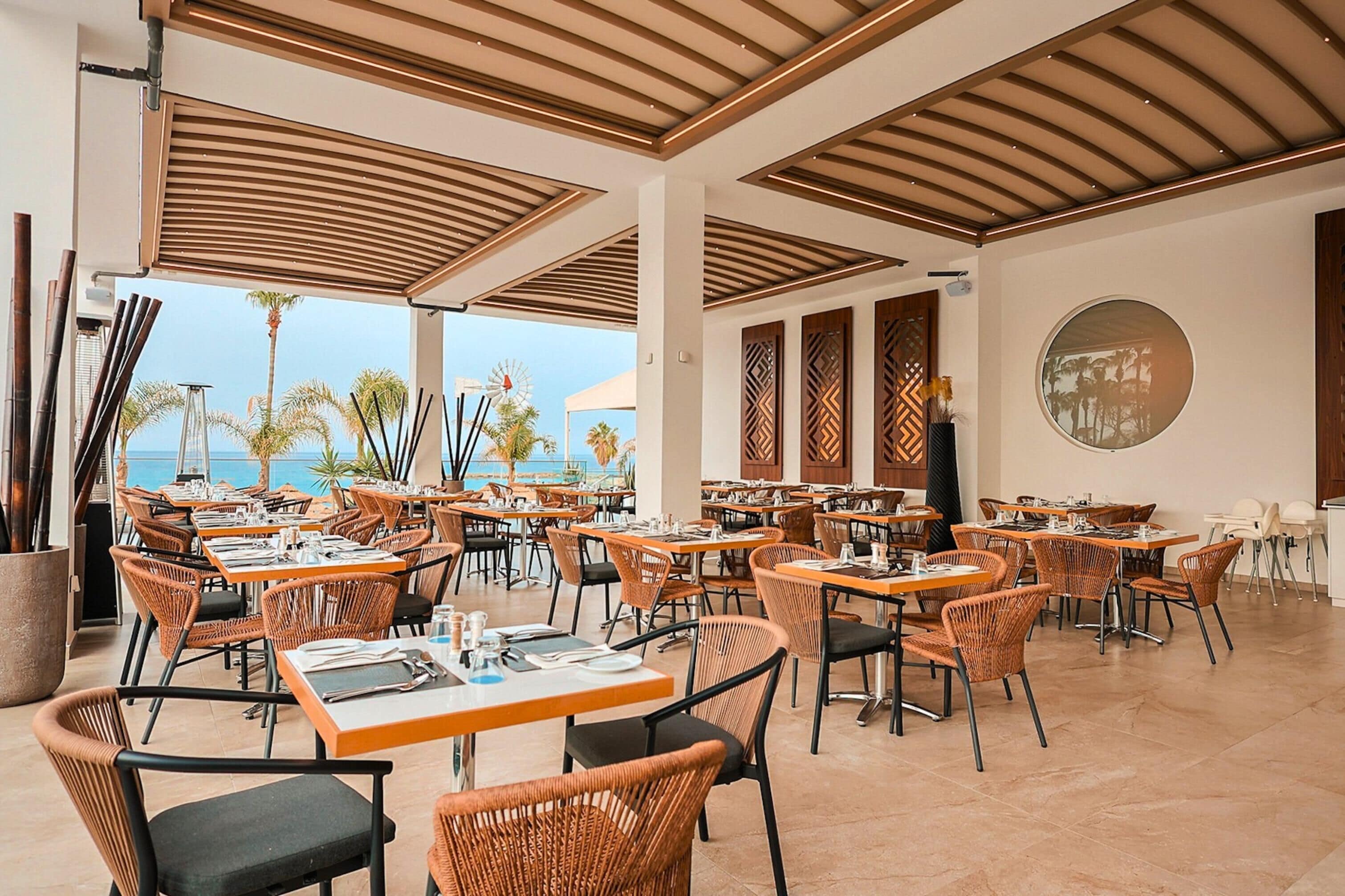 A spacious outdoor dining area with tables and chairs, a view of the sea, and a modern ceiling design.