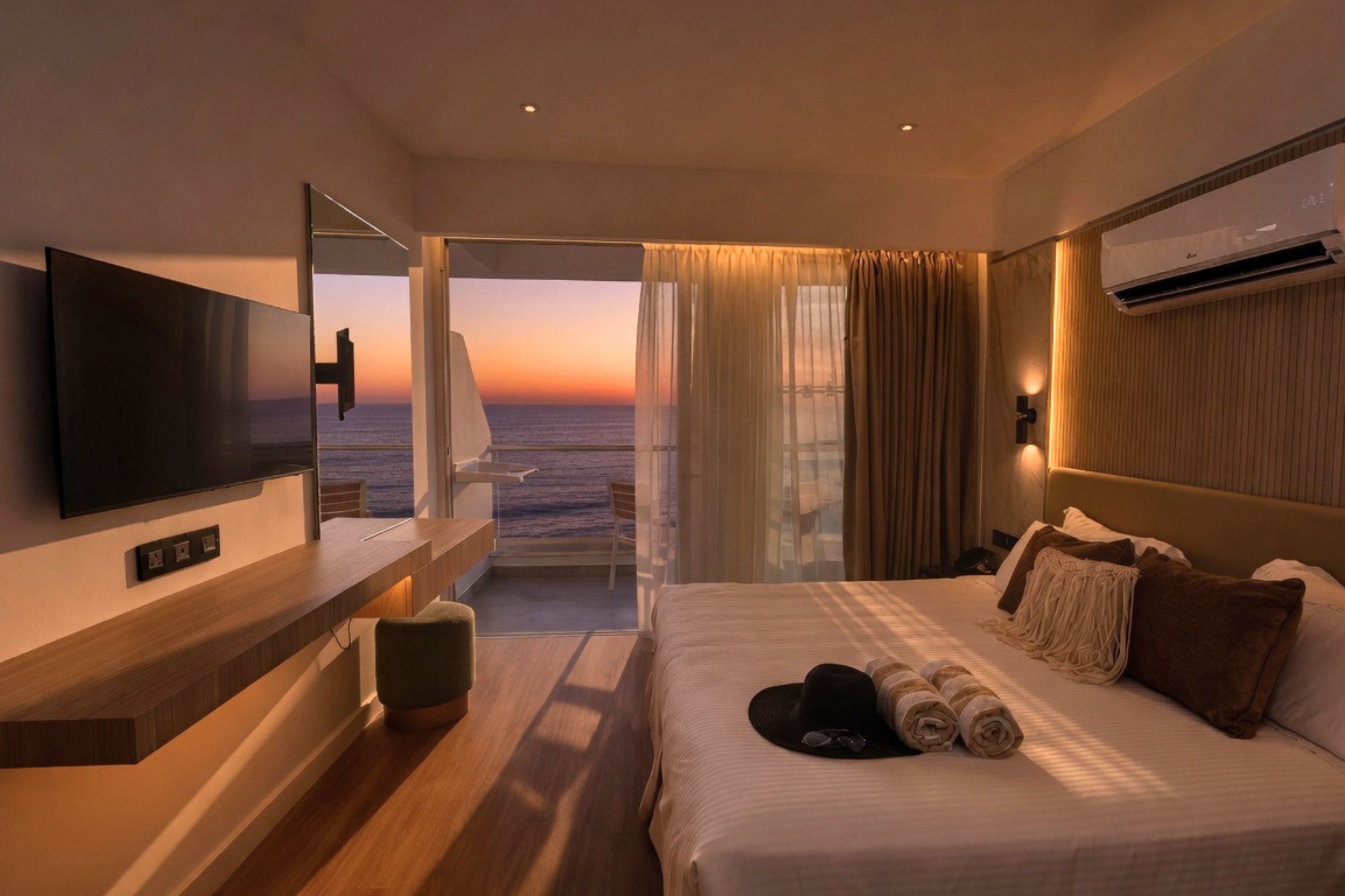 A hotel room with a bed, a TV, a desk, and a view of the ocean.