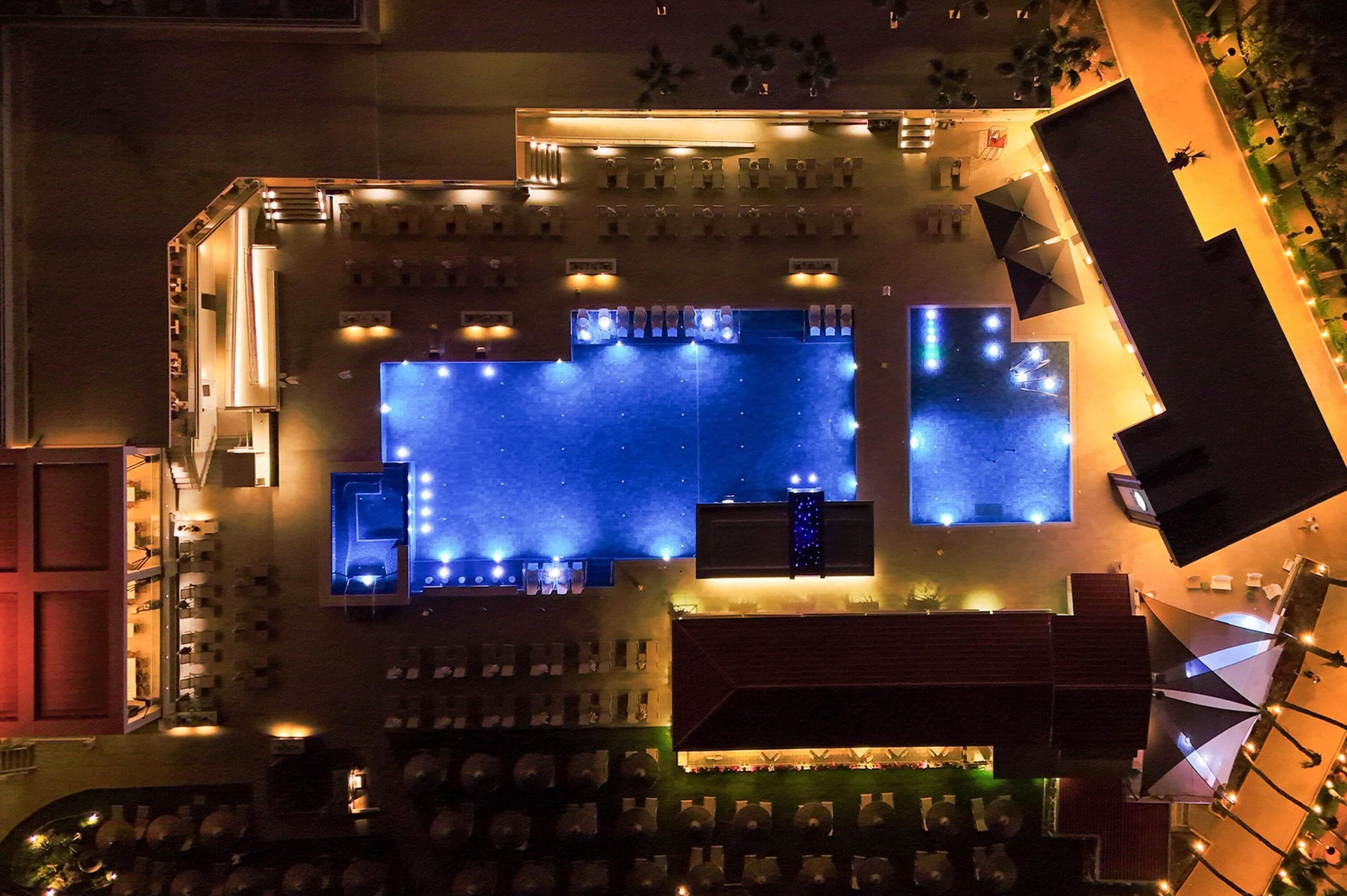 An aerial view of a hotel with a large outdoor pool, multiple dining areas, and a bar/lounge area.