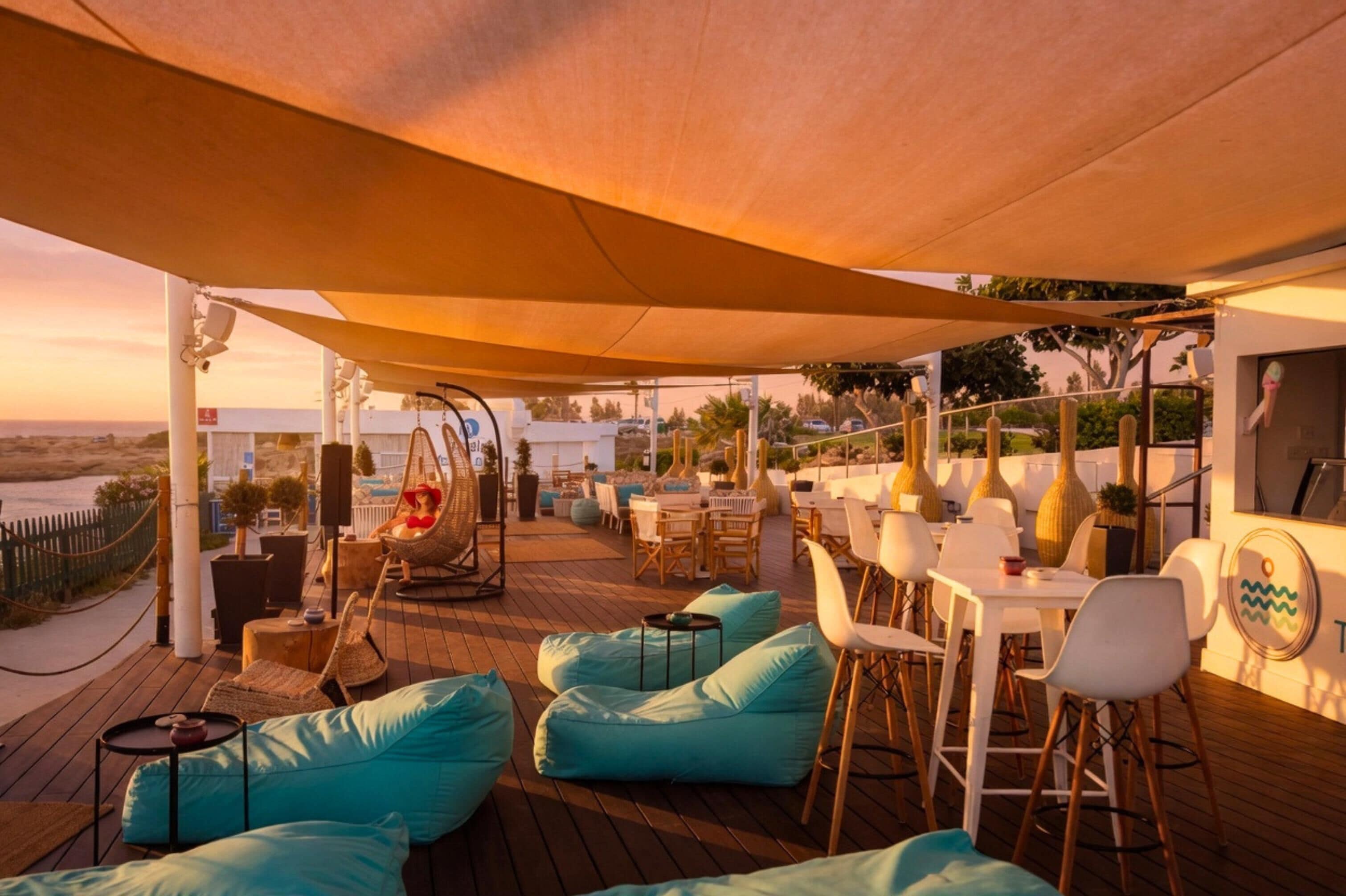 An outdoor seating area with tables and chairs, a swing, and a view of the beach.