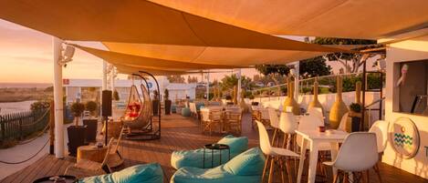 An outdoor seating area with tables and chairs, a swing, and a view of the beach.