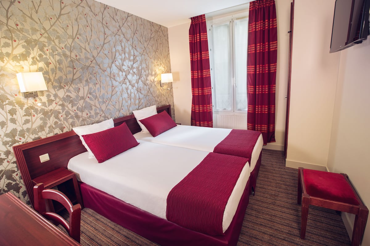 A hotel room with two beds, a wooden headboard, a small wooden chair, a red and white striped curtain, and a wall-mounted TV.