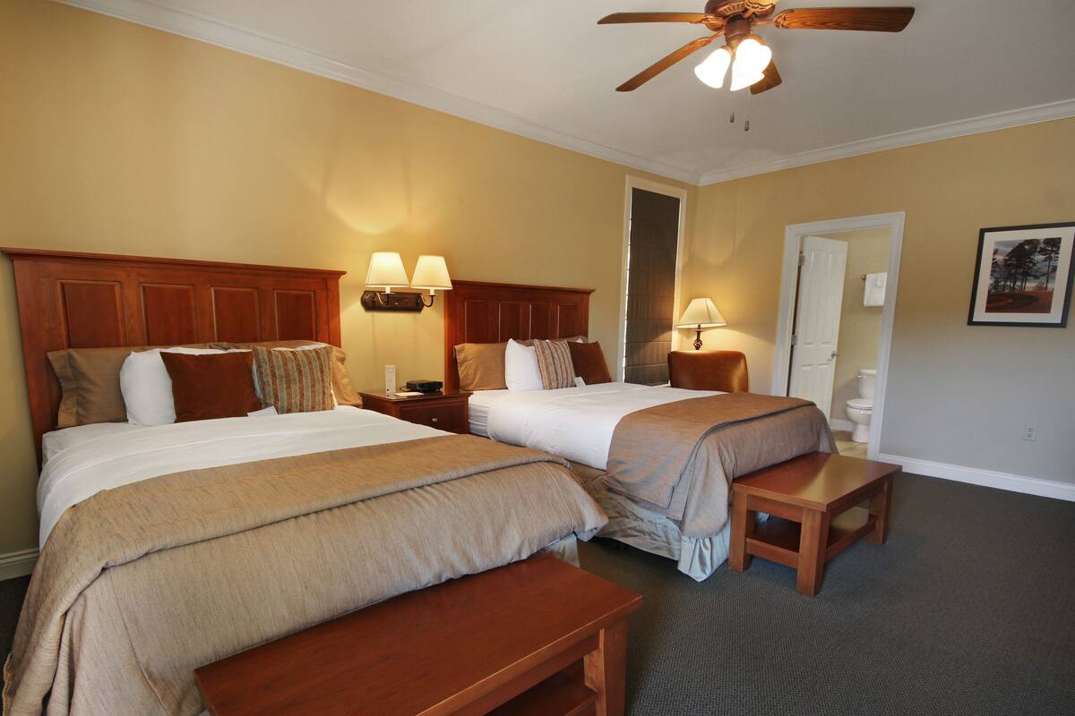 A hotel room with two beds, a ceiling fan, and a small wooden table.
