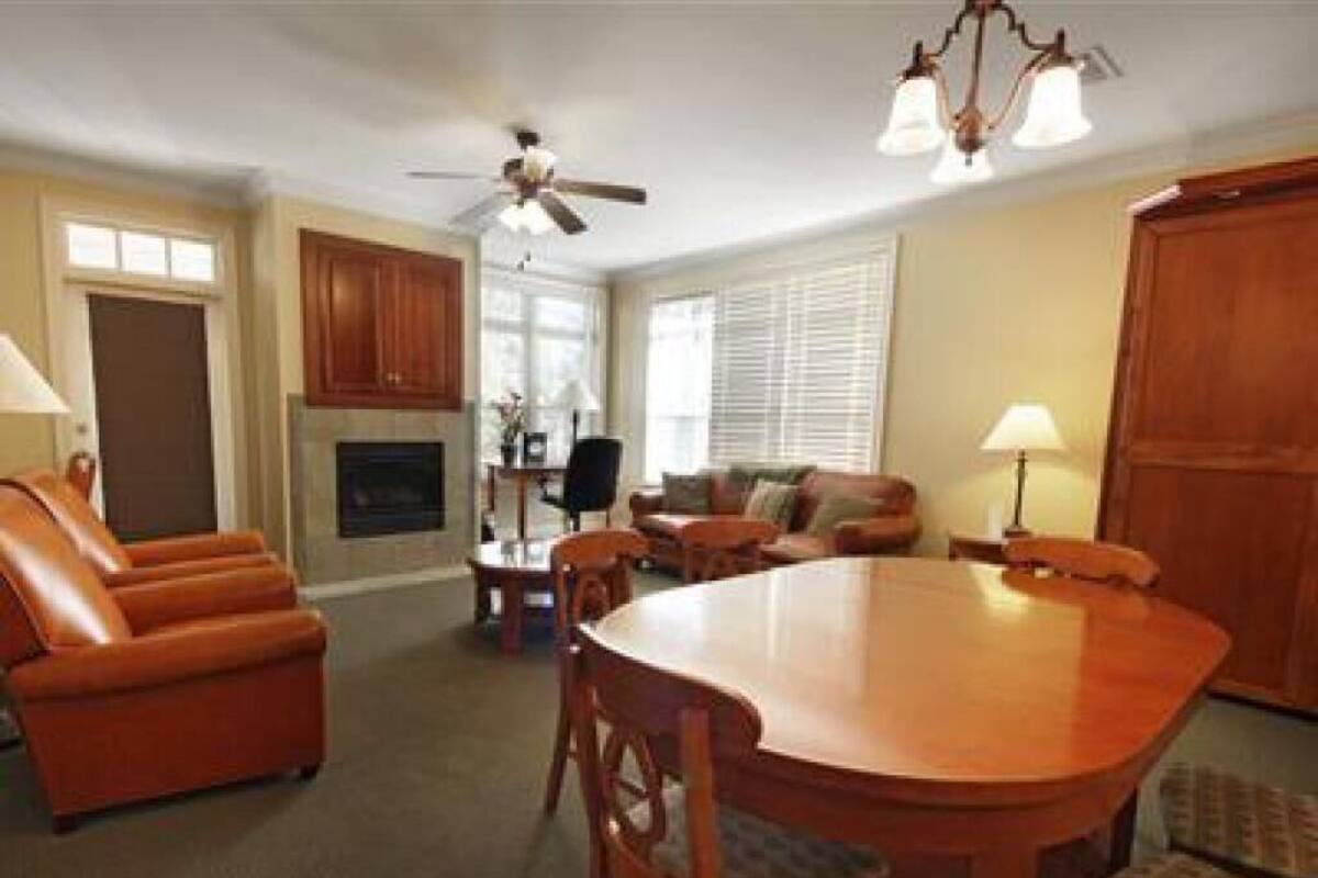 A spacious living room with a wooden dining table, leather chairs, a fireplace, and a ceiling fan.