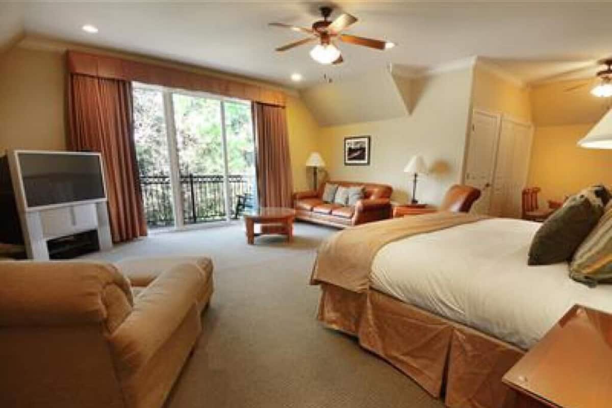 A hotel room with a large bed, a sofa, a TV, and a balcony with curtains.