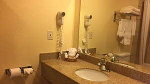 A bathroom with a granite countertop, a sink, a mirror, a towel rack, and two hair dryers mounted on the wall. - Turtle Bay Lodge (Redding)