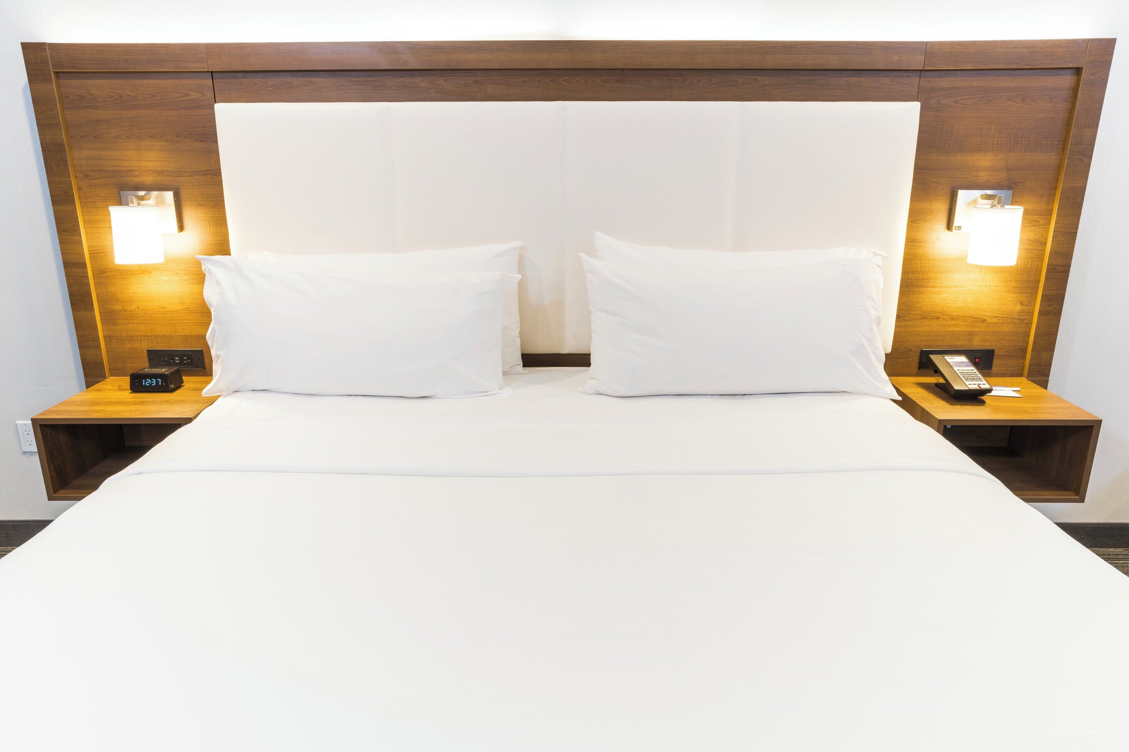 Quarto de hotel com uma cama grande, duas mesas de cabeceira e duas luminárias fixadas na parede.