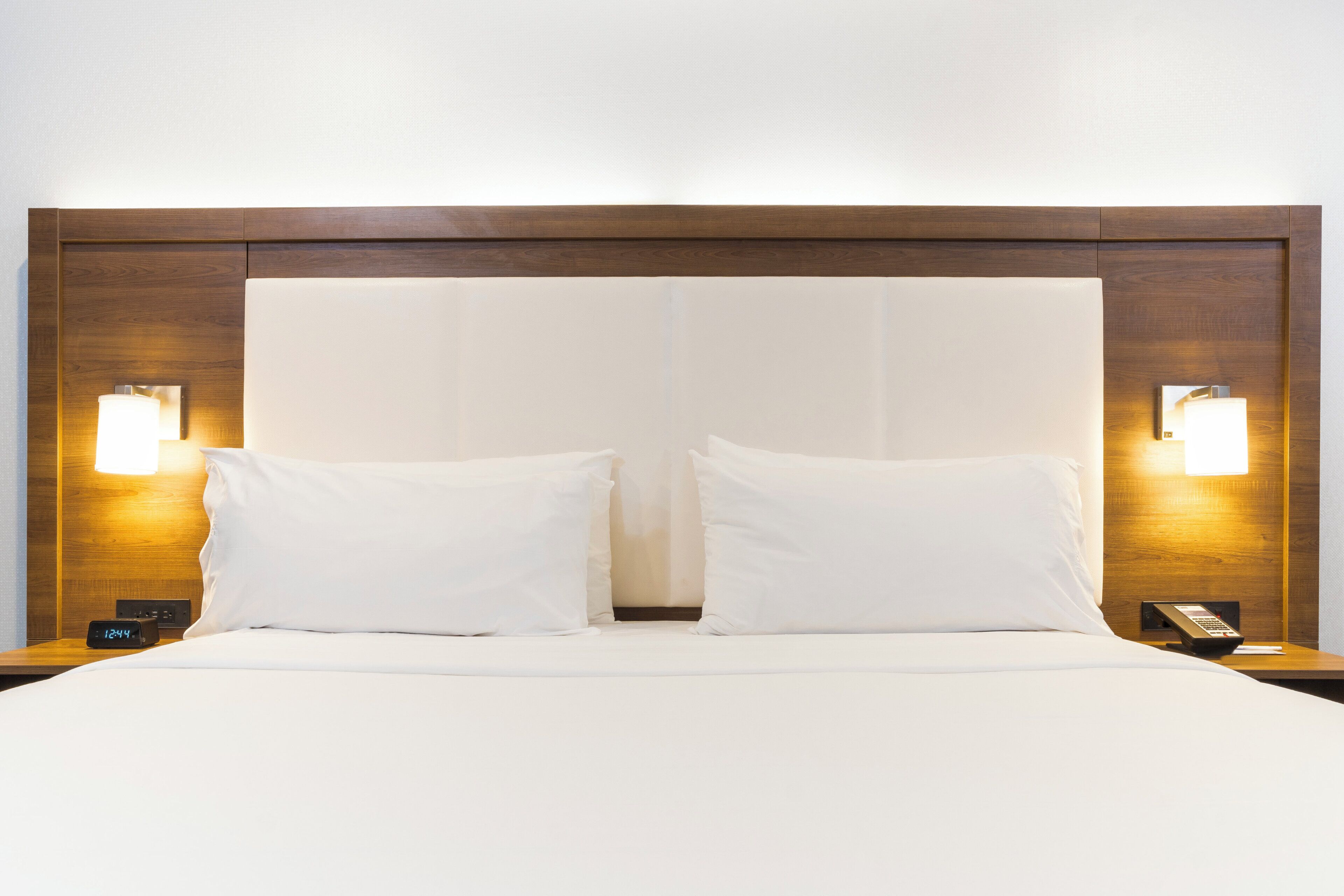 A hotel room with a large bed, two bedside lamps, and a nightstand with a phone and a digital clock.