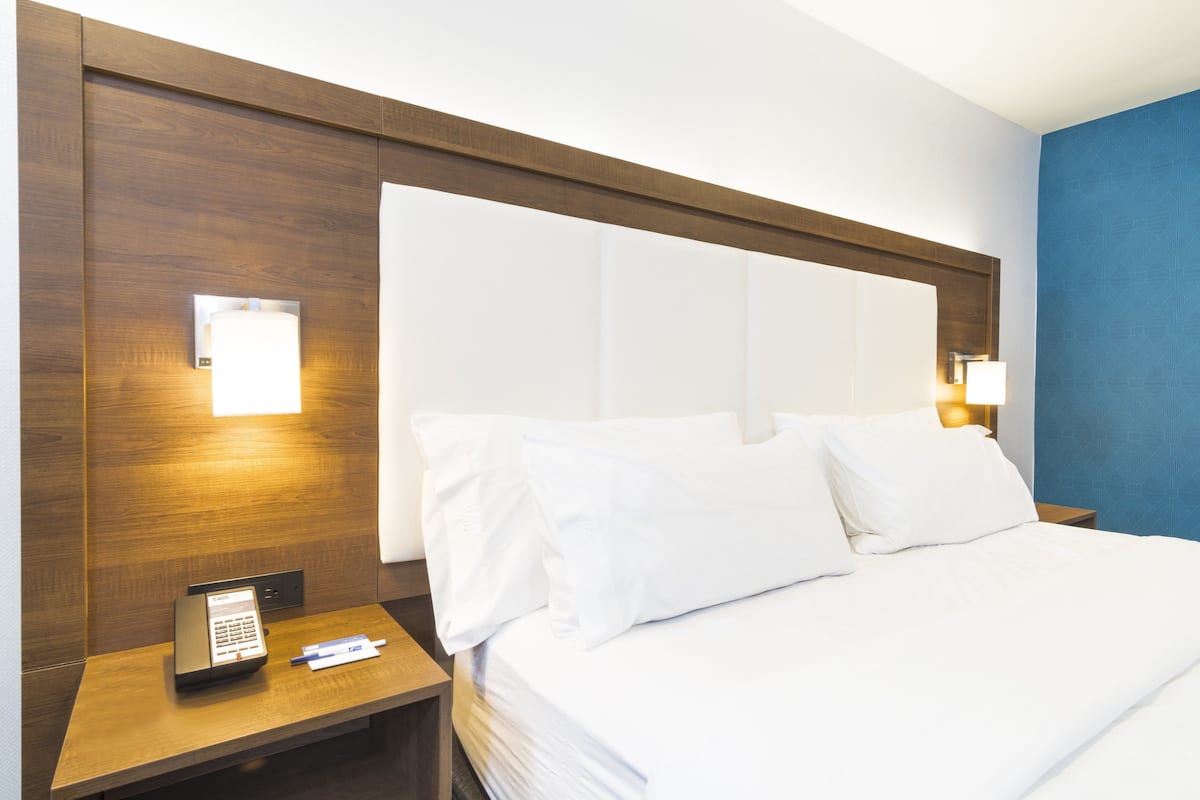 Une chambre d’hôtel avec une tête de lit en bois, une table de chevet avec un téléphone et un stylo, et un lit avec du linge de lit blanc.