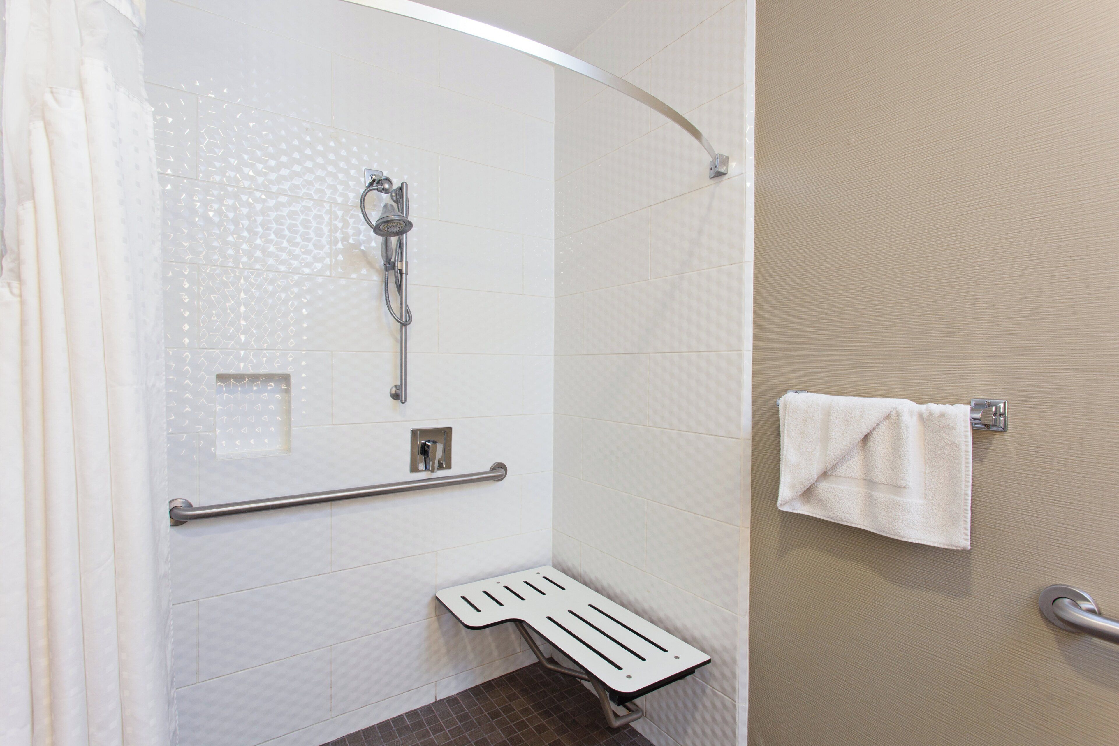A shower area with a handheld showerhead, grab bar, and a towel rack with a towel.