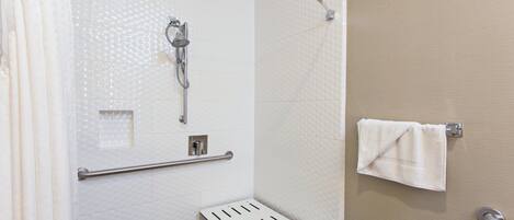 A shower area with a handheld showerhead, grab bar, and a towel rack with a towel.