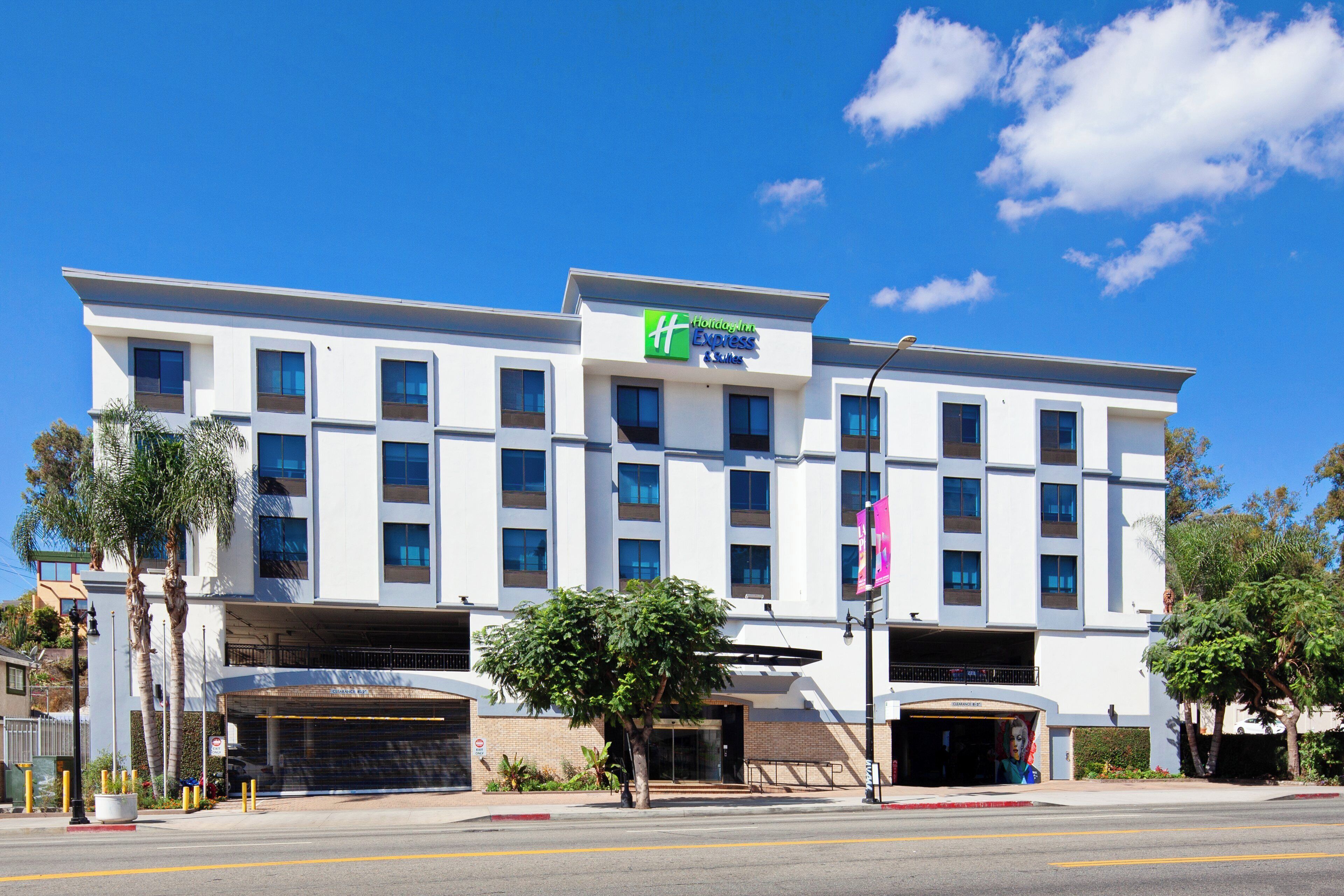 Un hotel Holiday Inn Express & Suites con un diseño moderno, varios estacionamientos y un cielo azul despejado.
