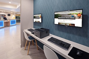 A modern hotel reception desk with a computer, printer, and a flat-screen monitor displaying a website. - Holiday Inn Express Hotel & Suites Hollywood Walk of Fame by IHG (Los Angeles)