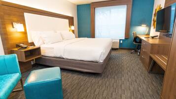A hotel room with a large bed, a desk with a chair, a TV, and a window with a view of palm trees.