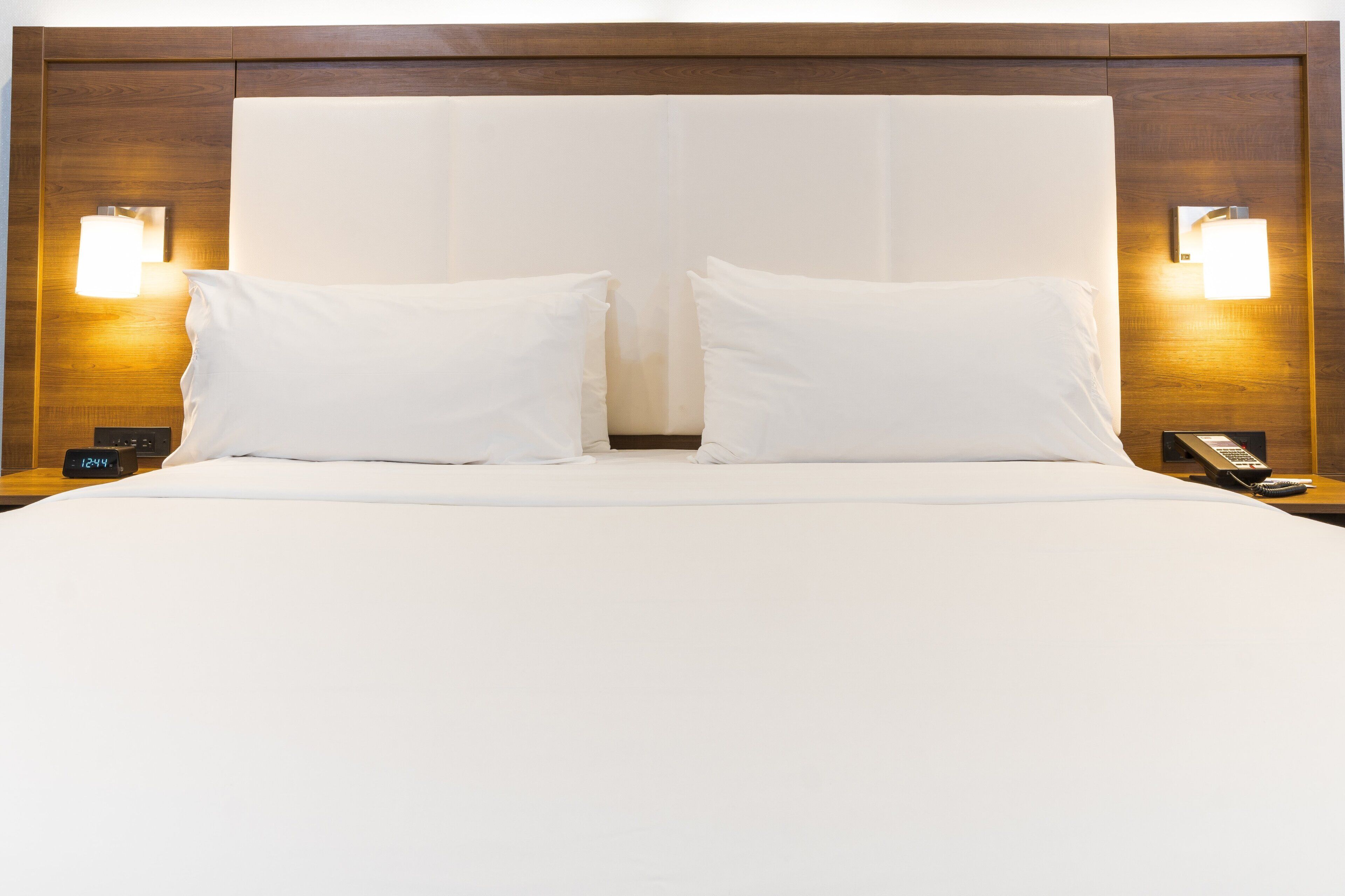 A hotel room with a large bed, two bedside lamps, a bedside clock, and a telephone.