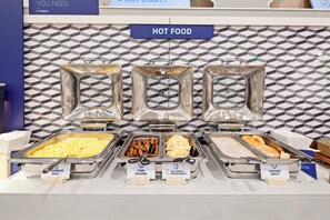 Een ontbijtbuffet met verschillende gerechten, waaronder roerei, varkensworst, omelet met eiwit en groenten, en worstsaus.