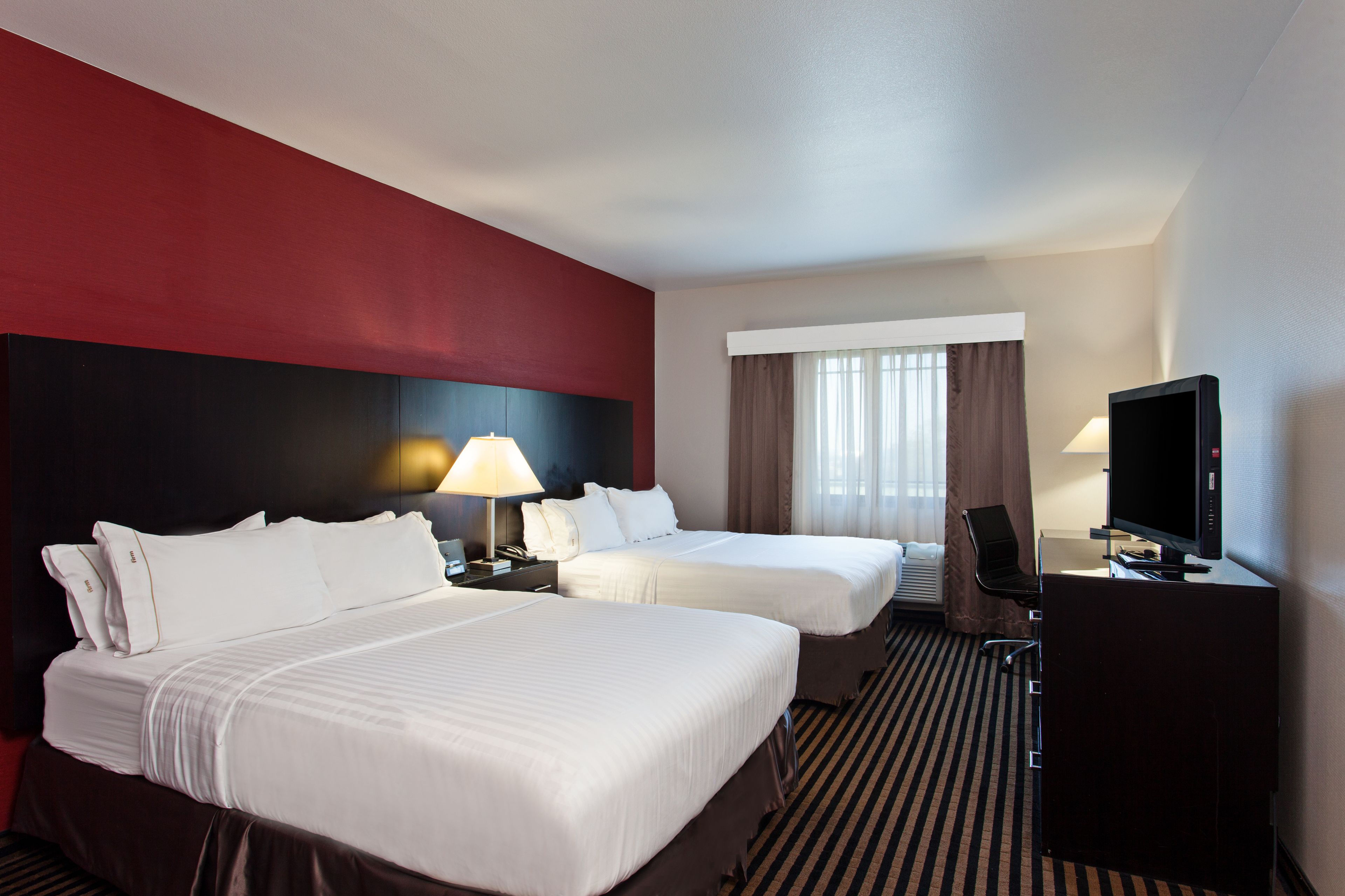 A hotel room with two beds, a desk with a TV, and a window with curtains.