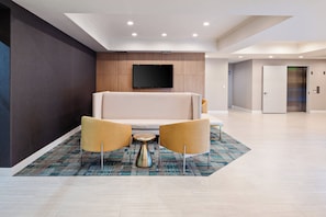 A modern lobby with a sofa, two armchairs, a coffee table, and a flat-screen TV mounted on the wall. - Holiday Inn Express Hotel & Suites Hollywood Walk of Fame by IHG (Los Angeles)