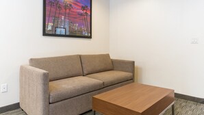 Una habitación moderna con un sofá color beige, una mesa de centro de madera y un cuadro con una vista urbana en la pared.
