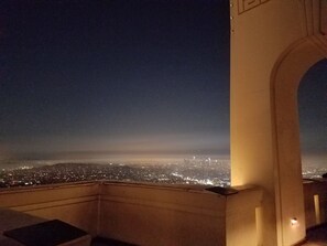 Een nachtelijk stadsbeeld, zichtbaar door een rondboogvenster, met een verafgelegen stadshemel vol lichtjes.