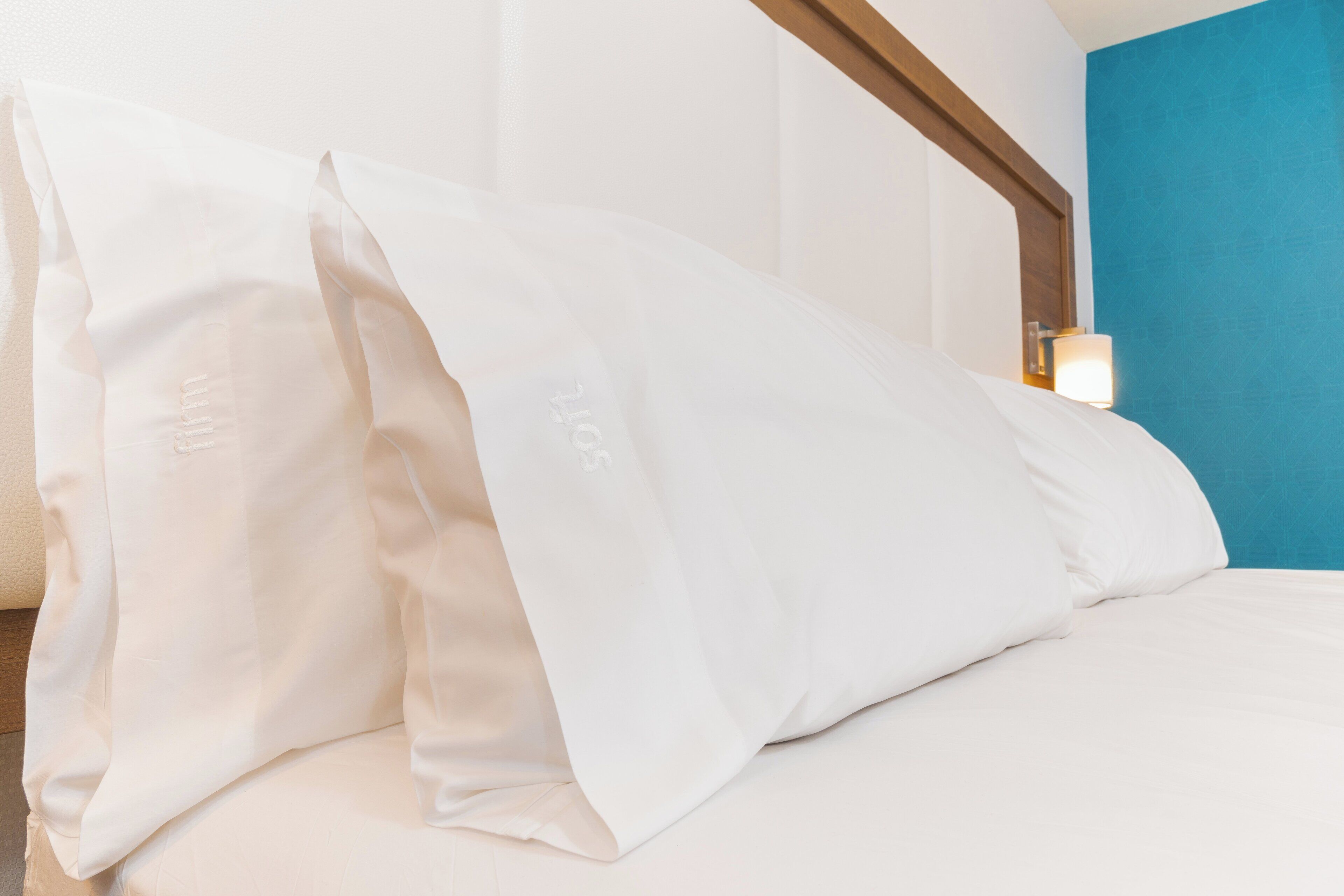 Una cama con ropa blanca y almohadas, cabecera de madera y pared de acento azul.