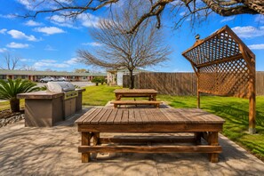 Eine Außenpatio-Terrasse mit Grill, Picknicktisch und Holzzaun.