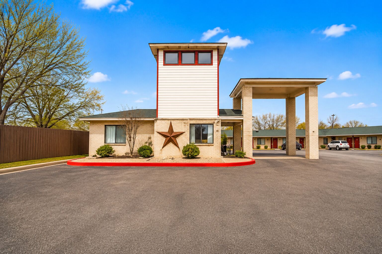 A motel with a central tower, a parking lot, and a row of single-story buildings in the background.