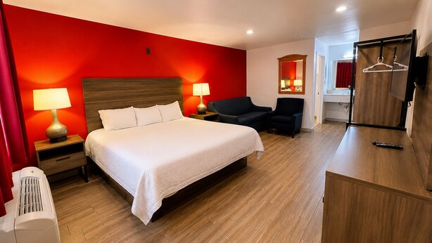 A hotel room with a large bed, two bedside lamps, a chair, a wardrobe, and a mirror. - Rose Park Inn & Suites I-10 East San Antonio (San Antonio)
