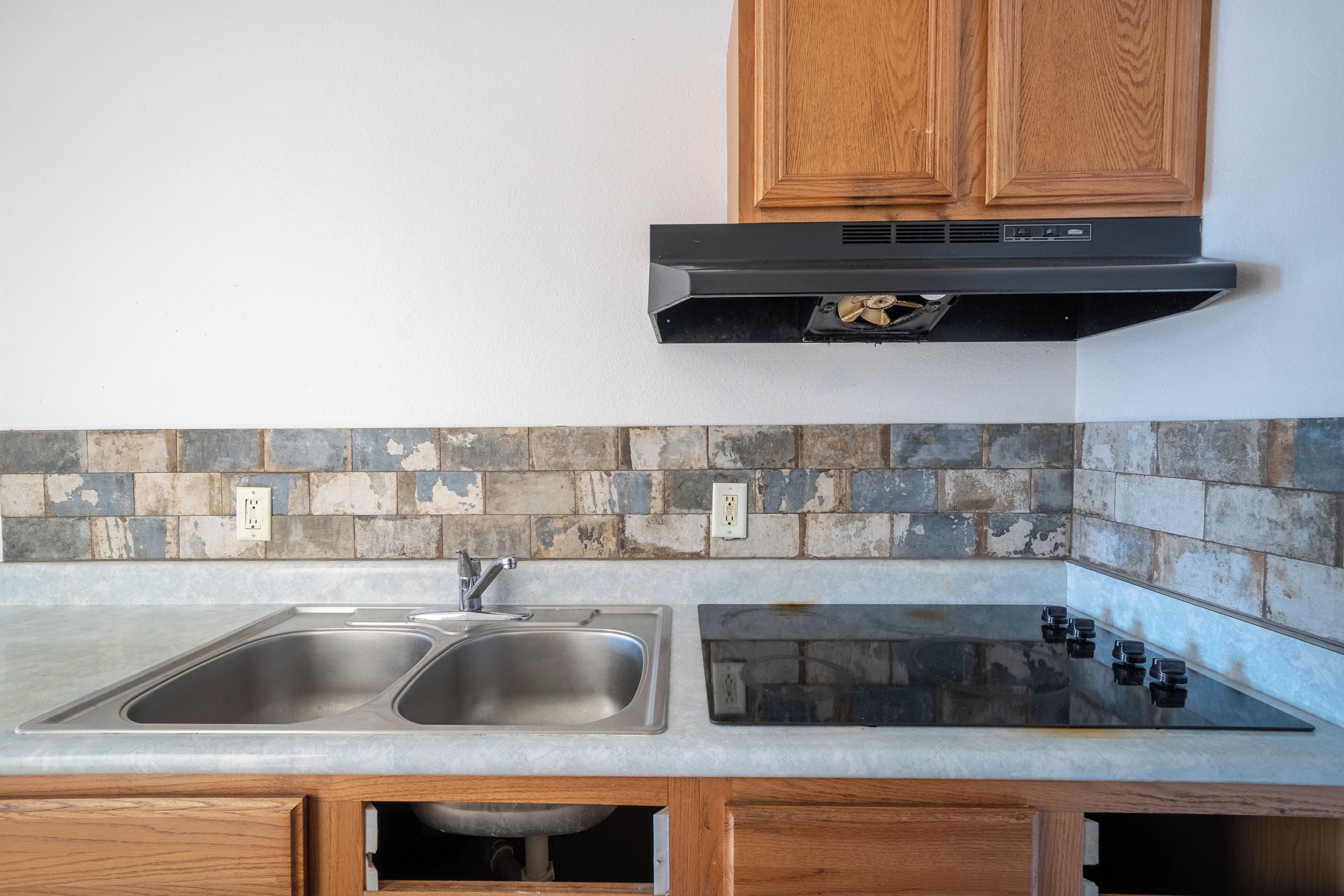 A kitchen with a double sink, a stove, wooden cabinets, and a stone backsplash.