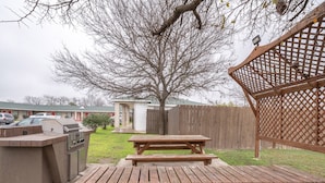 A backyard with a barbecue area, picnic table, and a wooden fence.