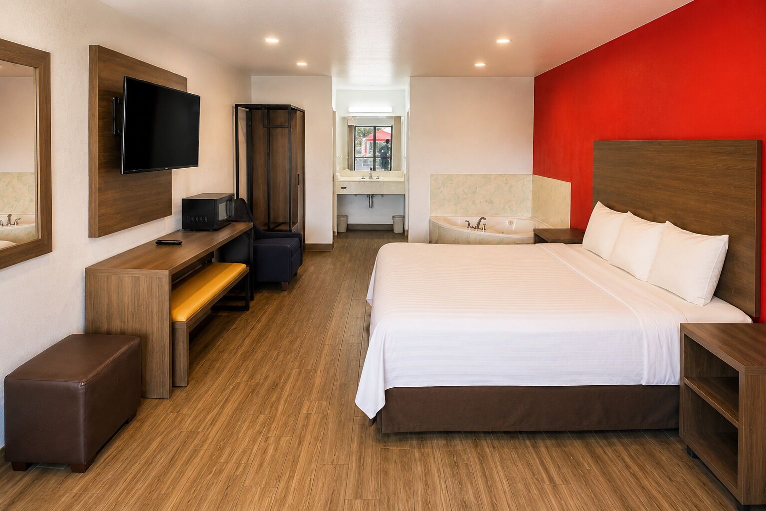 Una habitación de hotel con cama, escritorio, televisor y una pared de acento roja.