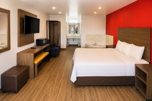 A hotel room with a bed, a desk, a television, and a red accent wall. - Rose Park Inn & Suites I-10 East San Antonio (San Antonio)