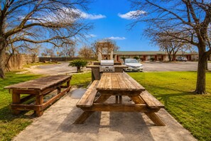 A picnic area with two wooden tables and a grill, surrounded by trees and a building in the background. - OYO Hotel San Antonio Near At&t Center (San Antonio)
