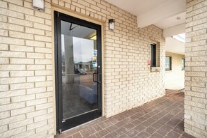 A building entrance with a glass door, a brick wall, and a small window. - OYO Hotel San Antonio Near At&t Center (San Antonio)