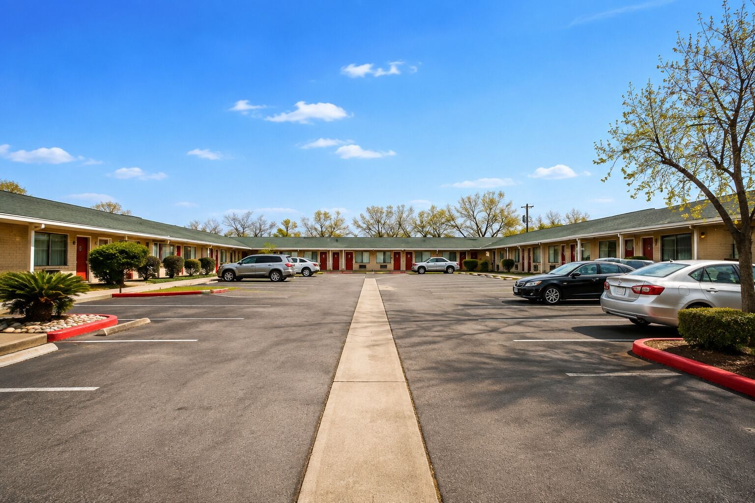 Un motel con estacionamiento central, varias habitaciones y cielo despejado.