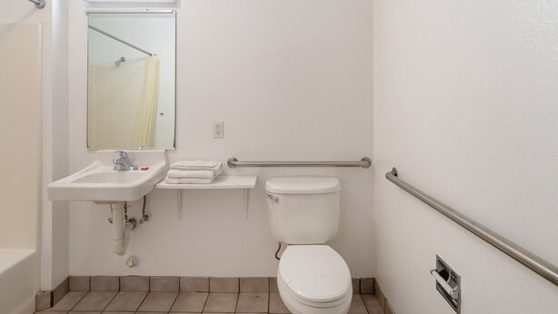 Un baño estándar con lavabo, espejo, inodoro y barras de apoyo.