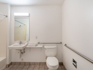 Un baño estándar con lavabo, espejo, inodoro y barras de apoyo.