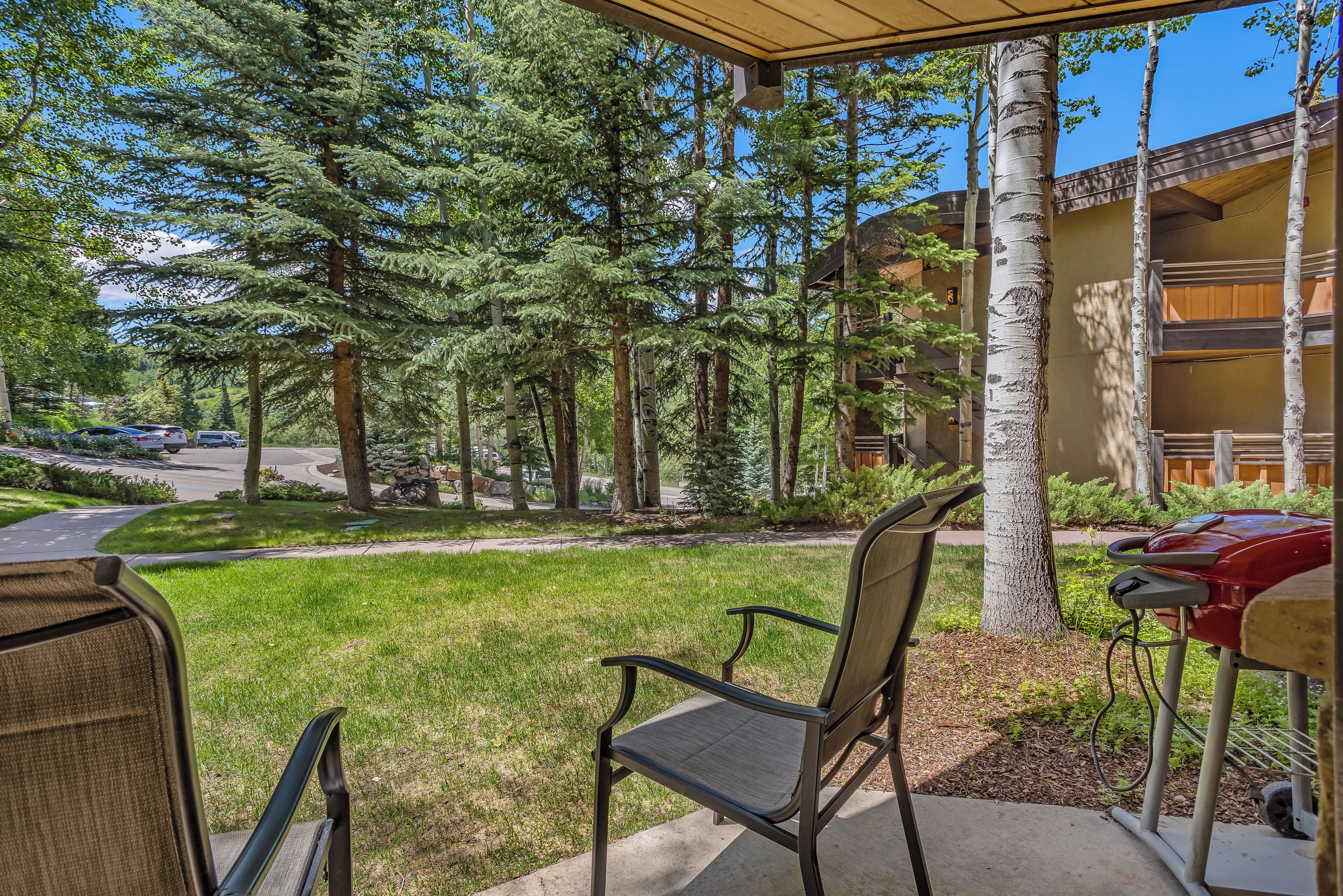 A covered outdoor seating area with chairs, a barbecue grill, and a view of a parking lot and trees.