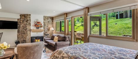 Quarto espaçoso com uma cama grande, lareira de pedra, sofá confortável e vista para um jardim exuberante.