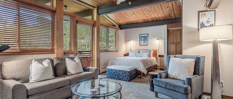 A cozy room with a sofa, armchair, and ottoman, a bed with a blue and white patterned cover, and a ceiling fan.