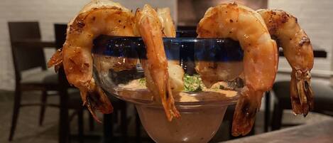 A glass bowl with grilled shrimp on a wooden table.