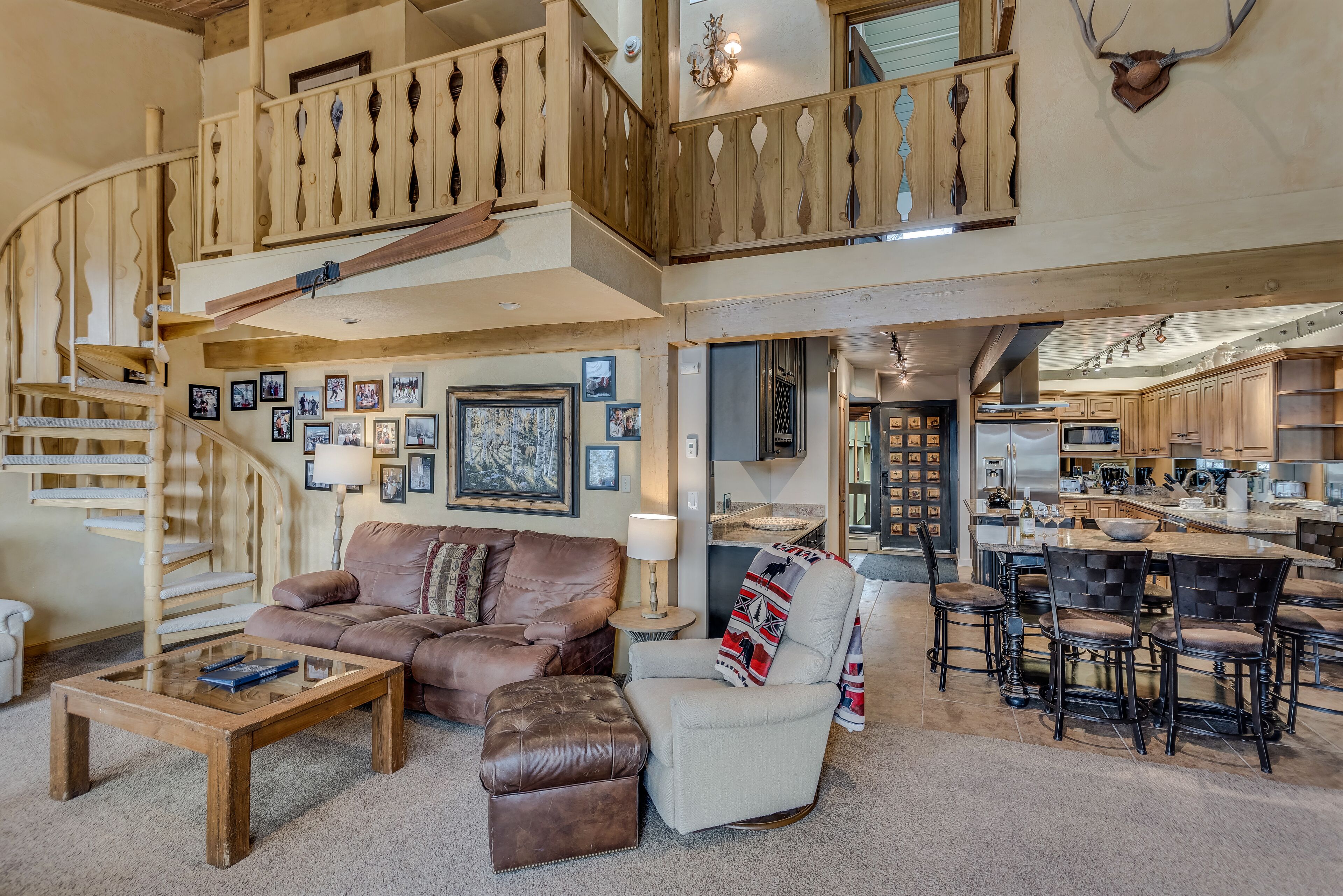 A spacious living area with a wooden staircase, a comfortable sofa, a coffee table, and a dining area with bar stools.