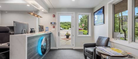 A reception area with a marble counter, leather chairs, a clock, and a view of greenery outside.