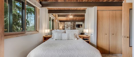 A bedroom with a large bed, wooden ceiling, stone wall, and a TV on the wall.