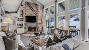 Una sala de estar acogedora con chimenea de piedra, asientos cómodos y ventanas amplias con vistas al exterior.