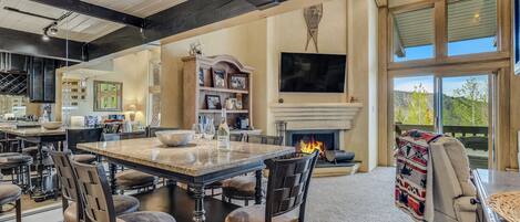 A spacious living area with a large dining table, comfortable seating, a fireplace, and a view of the outdoors.
