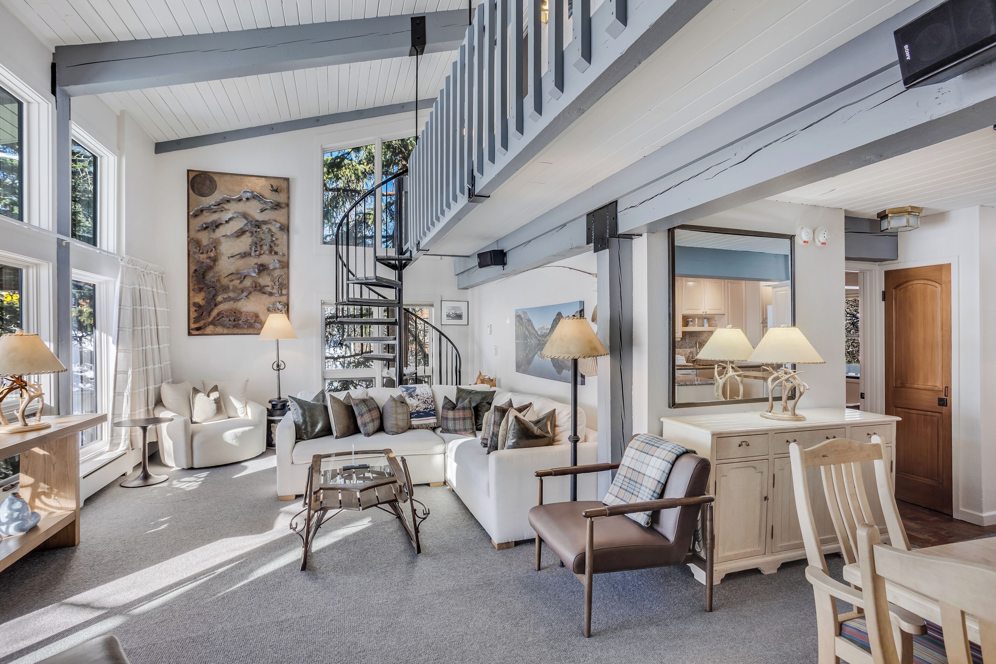 A spacious living room with a high ceiling, a staircase, and a large window.