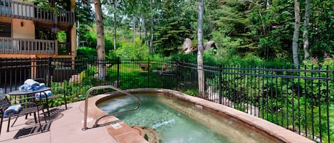 Jacuzzi rodeado por una cerca, con mesa de billar y sillas cerca.