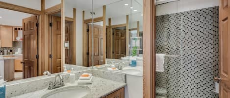 Un baño moderno con un espejo grande, encimeras de granito, ducha con mosaicos y armarios de madera.