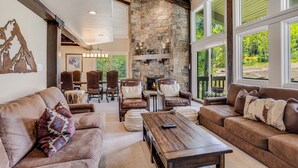 Un salón amplio con sofás de cuero, una chimenea de piedra y grandes ventanales con vistas al exterior.